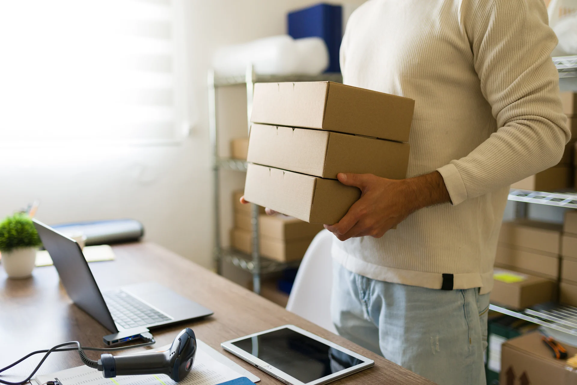 A man stood in front of his desk holding 3 boxes stacked on top of one another