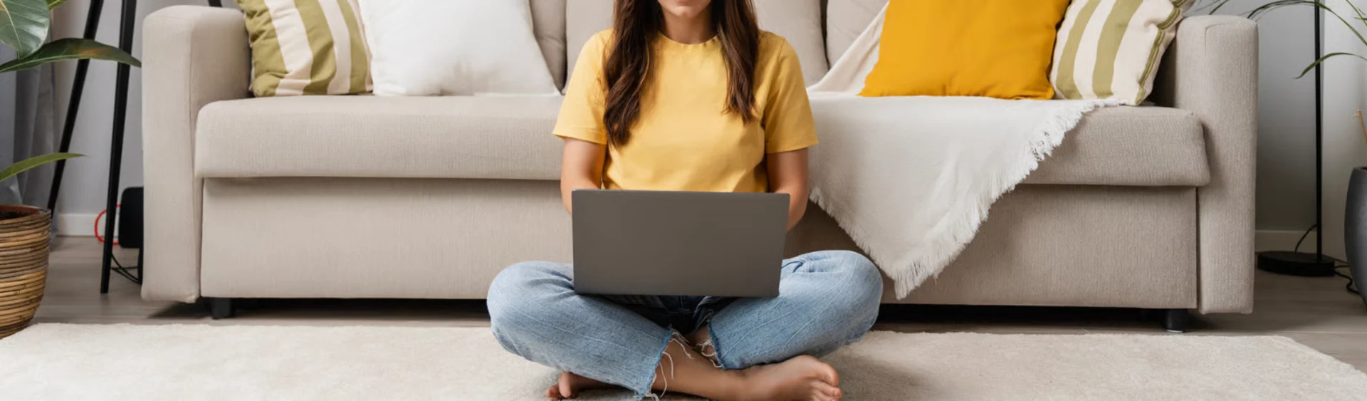 Person sitting down with a laptop in front of a sofa