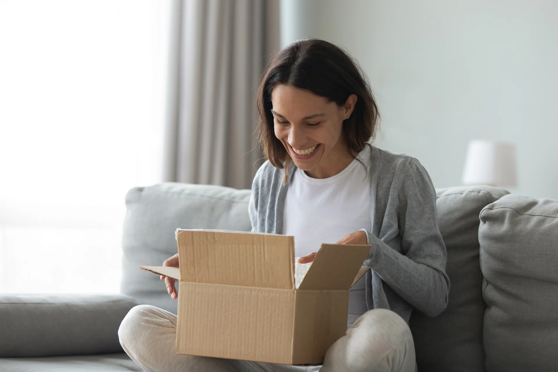 woman opening parcel on couch at home