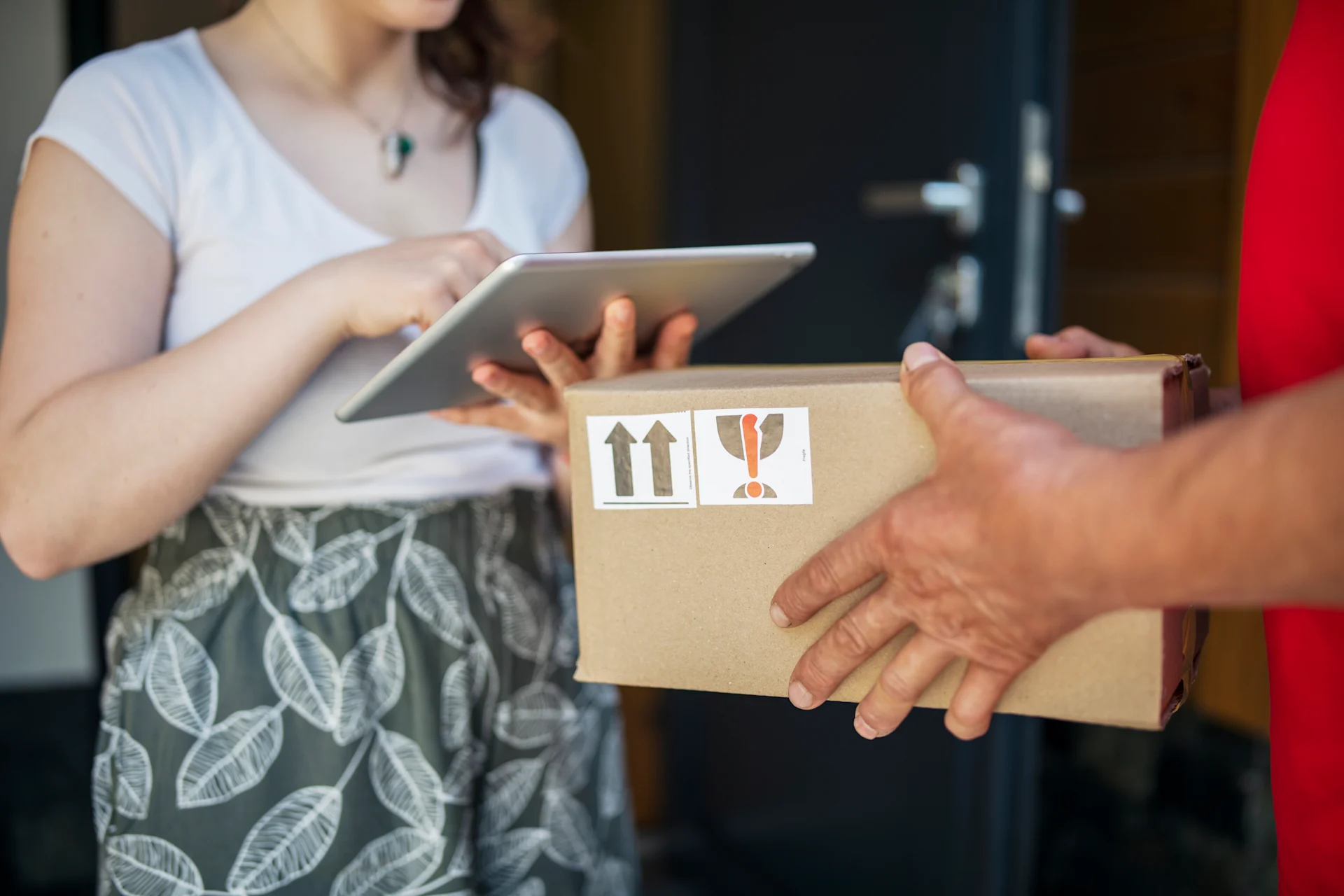 Woman on iPad collecting parcel off delivery man at door