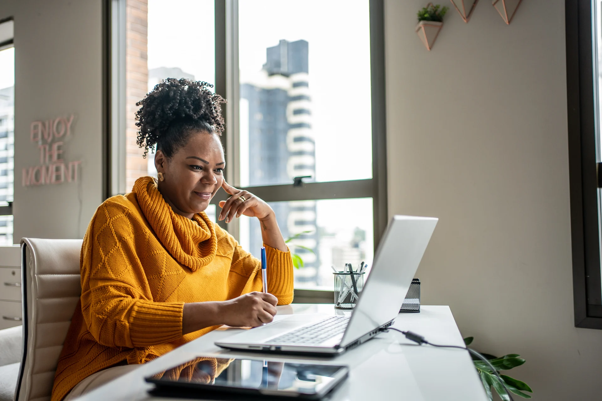 Woman using laptop at home and writing notes