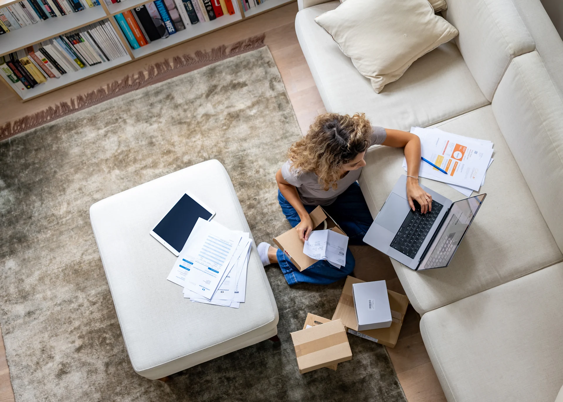 Overhead shot of woman using laptop and packing parcel for home business