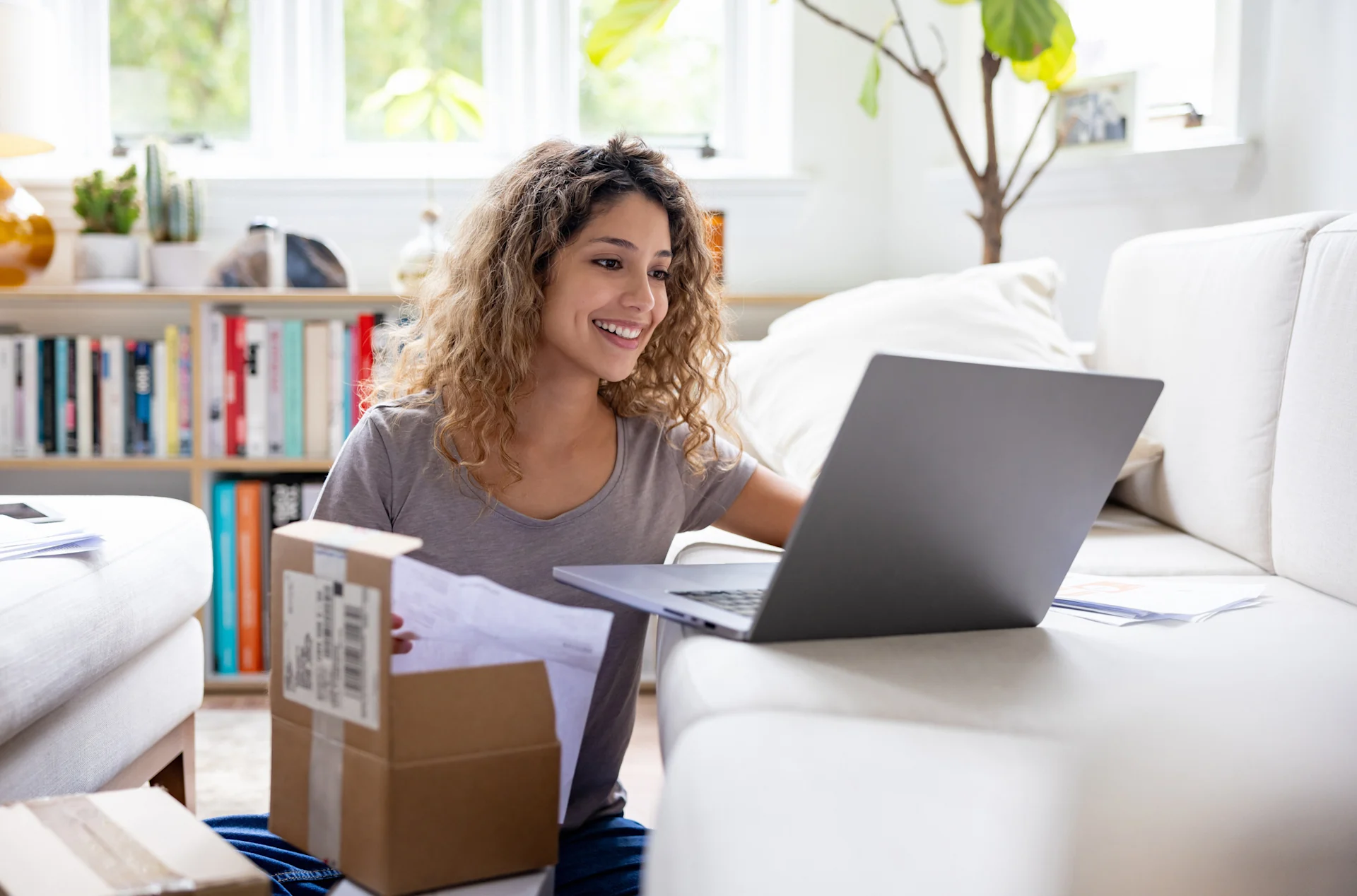 Woman smiling on laptop whilst packing parcel