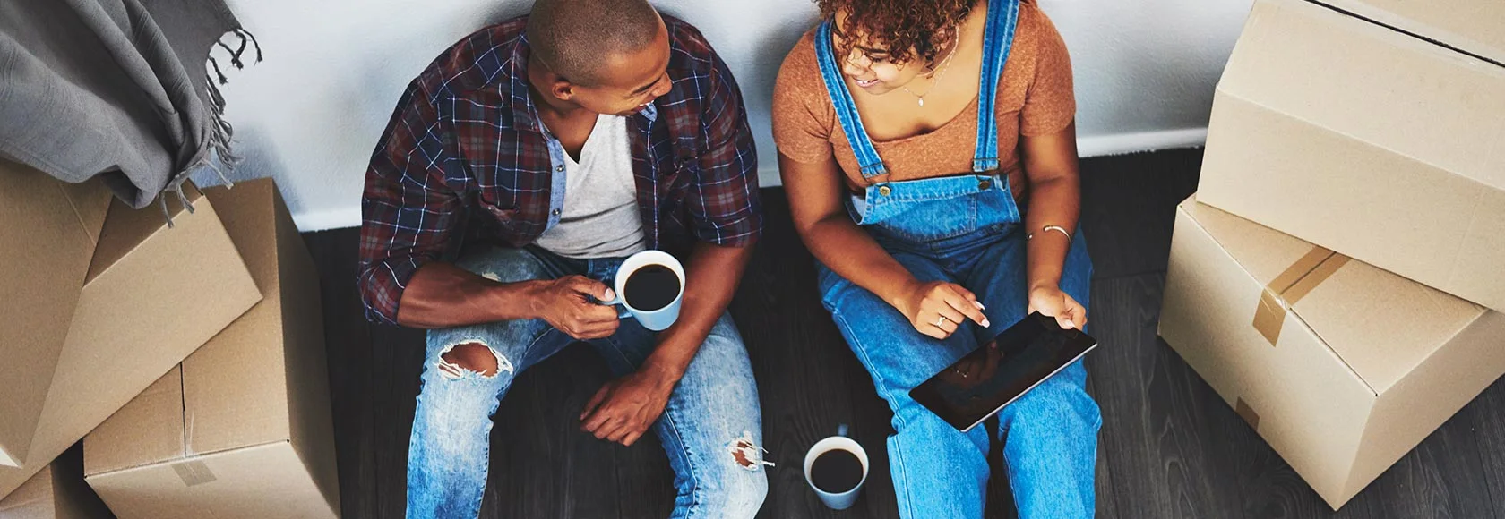 2 people sat on the floor drinking coffee with boxes around them