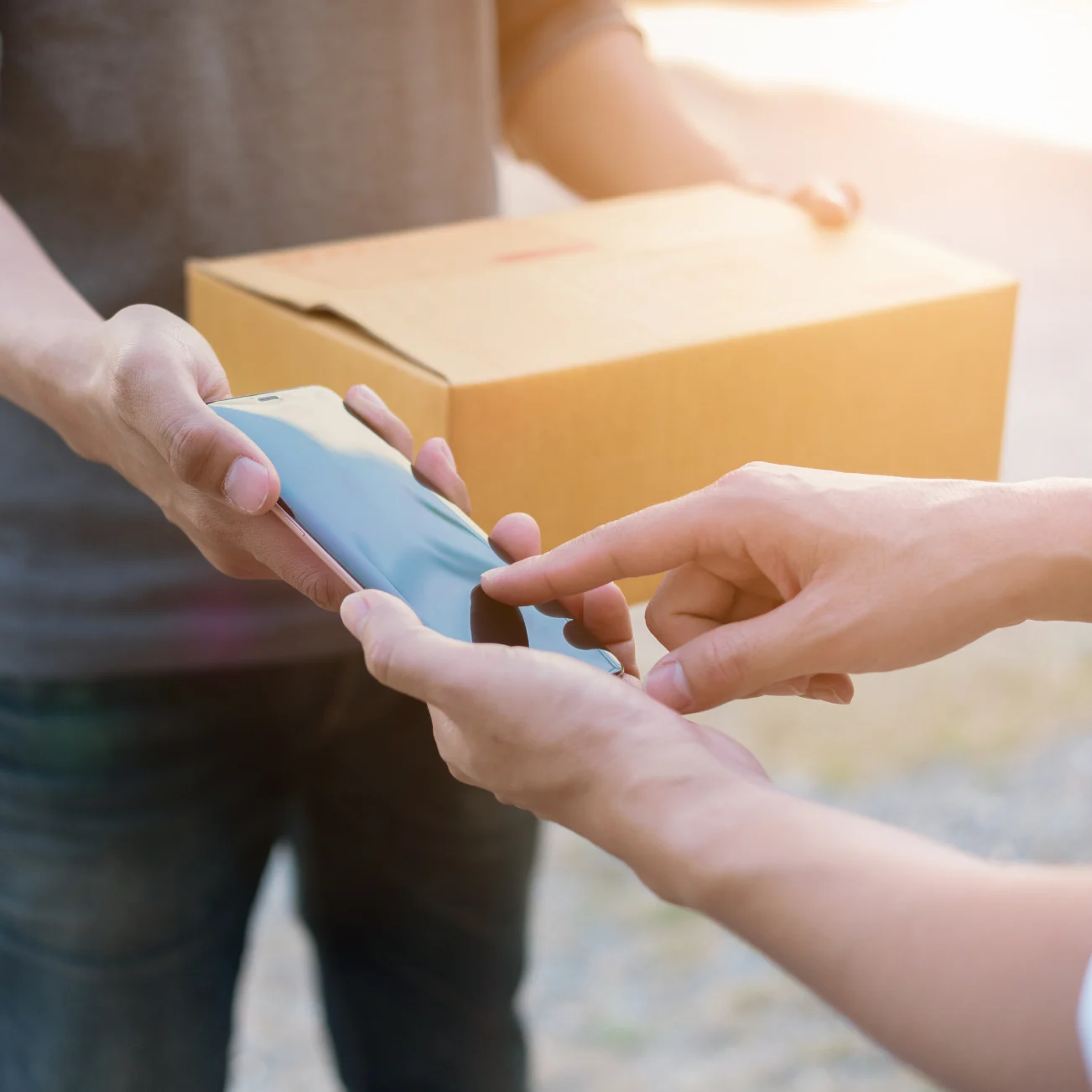 Deliveryman holding box and mobile phone out for recipient of parcel to sign with finger
